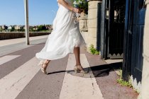 Sezione bassa della sposa in abito leggero tenendo bouquet luminoso ed entrando in chiesa . — Foto stock