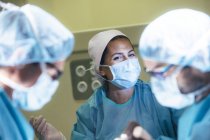 Donna ridente in uniforme chirurgo guardando i medici in sala operatoria — Foto stock