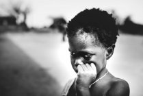 Goree, Senegal - 6 de diciembre de 2017: Retrato de un niño frotándose la cara y mirando hacia otro lado pensativamente . - foto de stock