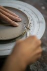 Immagine ritagliare di mani di vasaio femminile modellare bordo piatto di argilla con strumento — Foto stock
