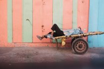 Side view of man sleeping on cart by colorful wall. — Stock Photo