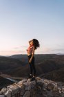 Стильная девушка с курчавыми волосами позирует на смотровой террасе в горной местности — стоковое фото