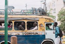 Goree, Senegal- 6 de diciembre de 2017: Vista lateral del hombre caminando en autobús por la ciudad mientras los pasajeros del autobús lo miran . - foto de stock