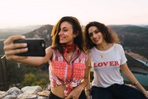 Dos mujeres sonrientes tomando selfie sobre paisaje impresionante - foto de stock