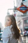 Brunette girl in casual clothes looking over shoulder at camera near underground — Stock Photo