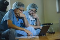 Vista lateral de dos hombres en uniforme médico mirando perplejos mientras miran el ordenador portátil juntos . - foto de stock