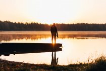 Silhouette de l'homme avec caméra à la main posant sur le bateau au lever du soleil scène sur le lac — Photo de stock