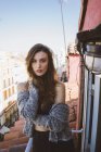 Confident brunette girl posing on balcony and looking at camera with hand on locks — Stock Photo