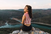 Stilvolle Frau sitzt auf Felsbrocken und bewundert Berglandschaft — Stockfoto