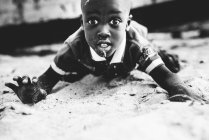 Goree, Sénégal- 6 décembre 2017 : Vue de face d'un garçon africain étonné allongé sur du sable et regardant une caméra — Photo de stock