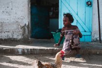 Yoff, Senegal- diciembre 6, 2017: Joven pobre niña sentada en la puerta de la casa en el pueblo . - foto de stock