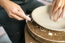 Crop image of artisan hands shaping clay plate edge with instrument — Stock Photo