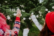 Crop  image of two girls decorating conifer with fairy lights. — Stock Photo