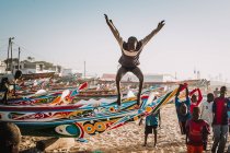 Yoff, Sénégal- 6 décembre 2017 : Groupe d'enfants africains s'amusant sur le rivage et sautant de voiliers peints lumineux . — Photo de stock