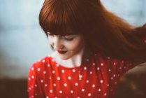 Redhead woman in red clothing and sunglasses waving hair andlooking down — Stock Photo