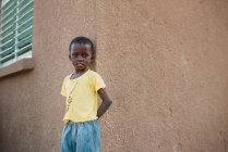 Yoff, Senegal - December 6, 2017: Portrait of little black boy leaning on wall at street — стоковое фото