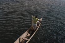 Goree, Senegal- Dezembro 6, 2017: Vista de baixo ângulo do homem de pé em barco de madeira e segurando rede de pesca . — Fotografia de Stock