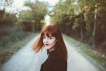 Redhead girl looking over shoulder at camera on rural road — Stock Photo