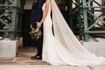 Braut im Brautkleid und Bräutigam mit Blumen posieren gemeinsam — Stockfoto