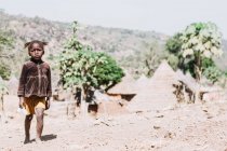 Гори, Сенегал - 6 декабря 2017 года: Девочка выглядит грустной во время прогулки по земле на фоне сельской деревни . — стоковое фото