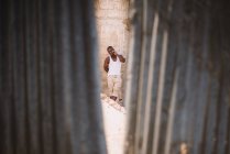 Goree, Senegal- 6 de diciembre de 2017: Disparo a través de la grieta en la pared de un hombre africano casual parado en la calle y haciendo gestos ante la cámara . - foto de stock