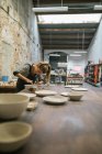 Side view of potter creating plates from white clay on table at workshop — Stock Photo