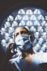 Высокоугловой вид хирурга в форме разговаривающего по смартфону за лампой на заднем плане — стоковое фото