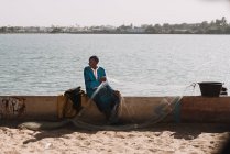 Goree, Senegal - 6 de diciembre de 2017: Hombre sentado con red de pesca en una cerca de hormigón a la luz del sol . - foto de stock