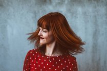 Экспрессивная рыжая девушка машет волосами на сером фоне — стоковое фото