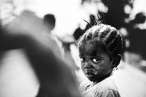 Kleines schmutziges Mädchen, das vor dem Hintergrund des Dorfes in die Kamera blickt. goree, senegal- 6. Dezember 2017: — Stockfoto