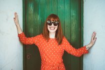 Smiling redhead girl in sunglasses posing at camera at doorway — Stock Photo