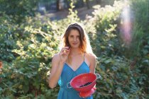 Portrait of blonde girl showing berries in bowl at sunlit garden — Stock Photo