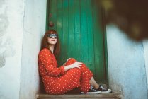 Red haired woman wearing red polka dots patterned dress posing at doorstep in doorway with green wooden door — Stock Photo