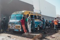 Goree, Senegal- 6 de diciembre de 2017: Grupo de personas africanas de pie alrededor de coloridos autobuses en una pequeña ciudad africana . - foto de stock