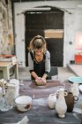 Концентрована жінка міняє глину на дерев'яному столі в майстерні — стокове фото