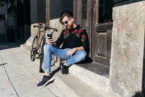Trendy man setting by bicycle and browsing smartphone — Stock Photo