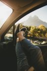 Crop female putting her legs out opened car window during countryside trip. — Stock Photo