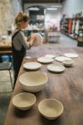 Hand maiden plates on table over potter working with clay on background — Stock Photo