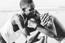 Yoff, Senegal- December 6, 2017: Side view of youngsters wrestling playfully on tropical shoreline. — Stock Photo