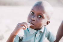 Yoff, Senegal- 6 de diciembre de 2017: Retrato de un niño africano lamiendo una bolsa de plástico y mirando a la cámara a la luz del sol . - foto de stock