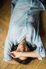 Brunette femme couchée sur le sol et gardant le bras sur le visage souriant — Photo de stock