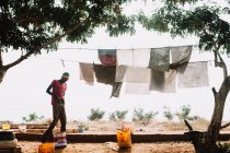 Goree, Senegal- December 6, 2017: Side view of man standing and putting on pants by drying clothes. — Stock Photo