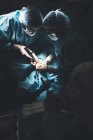 Groupe de chirurgiens opérant patient sous lampe lumineuse — Photo de stock