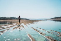 Mulher andando ao longo do lago azul no dia ensolarado — Fotografia de Stock