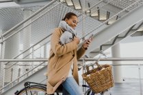 Вид сбоку женщины на велосипеде, обернутой в пальто и использующей смартфон — стоковое фото