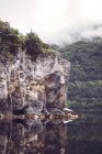Rocky cliff over lake with trees-covered hill slope — Stock Photo