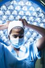 Retrato de la mujer con máscara en la sala de cirugía contra la lámpara y mirando dow - foto de stock