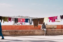 Goree, Senegal- December 6, 2017: View of man sitting on street of behind linen on rope in sunlight. — Stock Photo