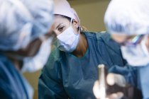 Retrato de mujer enmascarada viendo médicos operando en el hospital - foto de stock