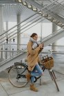 Jolie femme avec vélo de ville enveloppant dans un manteau et un smartphone de navigation — Photo de stock